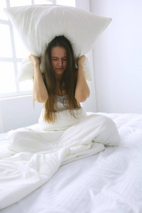 年轻的白种女人用枕头遮住头和耳朵