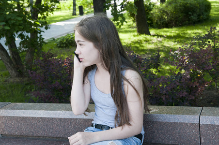 年轻迷人的女孩说话, 电话在板凳上。夏日公园。微笑.照片