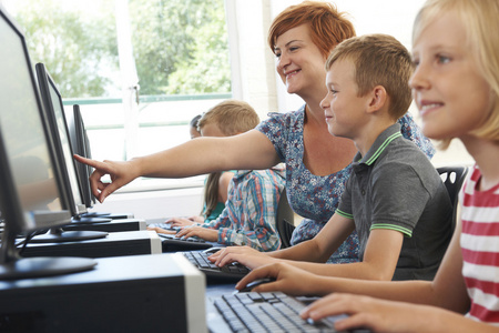 男小学学生在与老师的电脑课