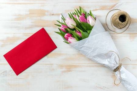 用白色纸和红色信封包裹的粉红色郁金香花束
