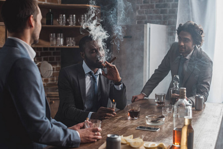 年轻的多民族商人在抽雪茄和喝威士忌时交谈