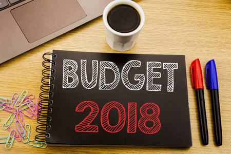 手写公告文本显示预算2018。家庭预算会计规划的商业概念写在笔记本上的木制背景在办公室与笔记本电脑咖啡