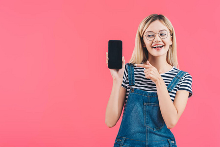 肖像微笑的女人在眼镜指向智能手机与空白屏幕上的粉红色