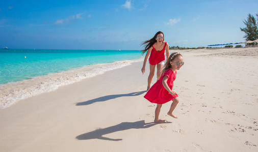 年轻的妈妈和小女孩奔跑在地处热带的海滩