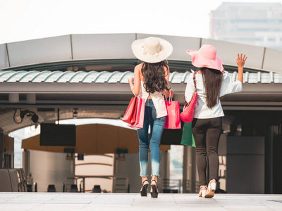 在购物包购物袋的年轻妇女的后视图, 亚洲女孩正在享受他们在城市的购买乐趣。消费主义与生活方式概念