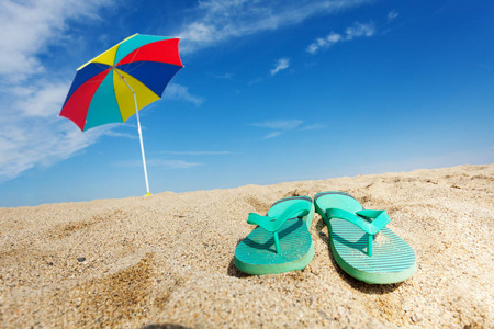 热带背景与翻转的拖鞋和太阳伞在沙滩上