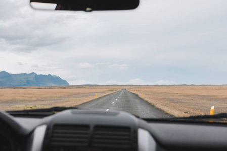 从车内观看在冰岛与山在背景的一条长的空的路前面