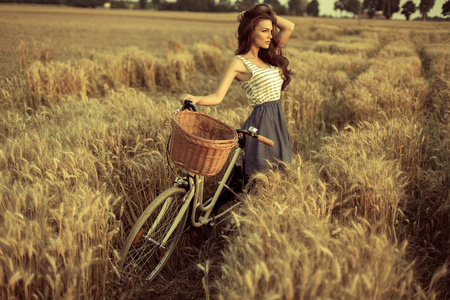 自行车在日落时在麦田上休息的女人