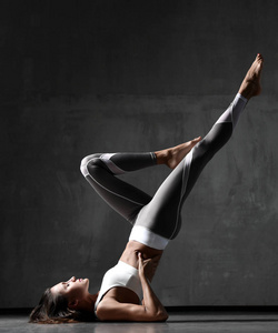 年轻的运动妇女做体操伸展健身锻炼在白色上衣和灰色裤子