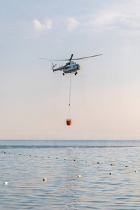 一架带红色篮子的直升飞机在海面上降下来捉水。