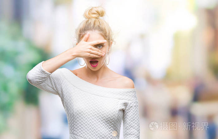 年轻美丽的金发碧眼的女人在孤立的背景偷看在休克覆盖脸和眼睛用手