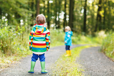 两个小兄妹男孩在五颜六色的雨衣和靴子走路