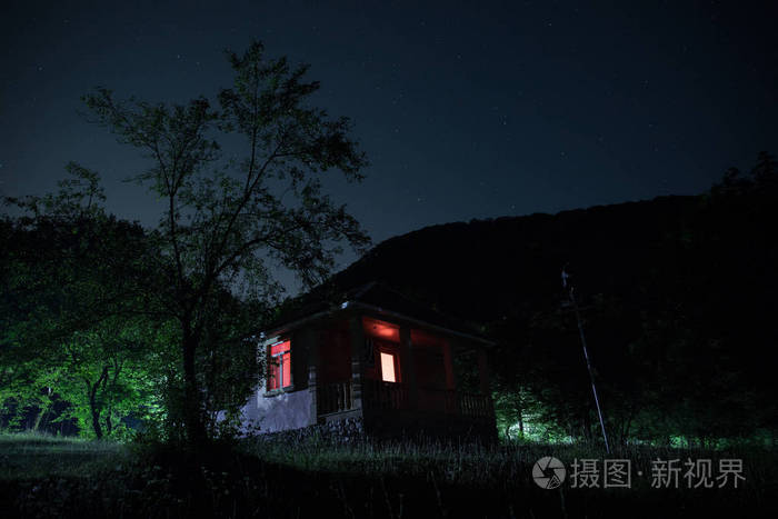 晚上在森林里建筑的山夜风景与月亮或老式乡下房子在晚上与云彩和星.