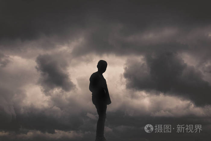 男孩剪影在云彩和黑暗的背景.孤独,自由,绝望或无助感