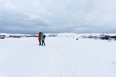 两个年轻的女孩在明亮的夹克旅行在雪苔原的白雪皑皑的山峰在冬天的霜冻淹没在雪中