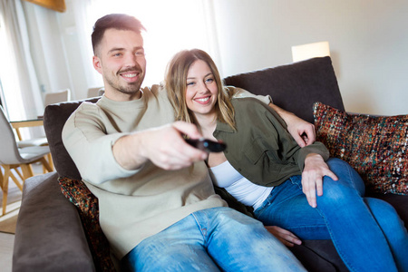 美丽的年轻的微笑的夫妇在家里的沙发上看电视