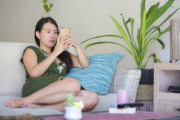年轻美丽和轻松的亚洲华人妇女躺在家里的客厅沙发沙发上使用互联网上