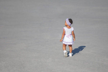穿着白色连衣裙的非洲小美国小孩正沿着人行道走。总体规划