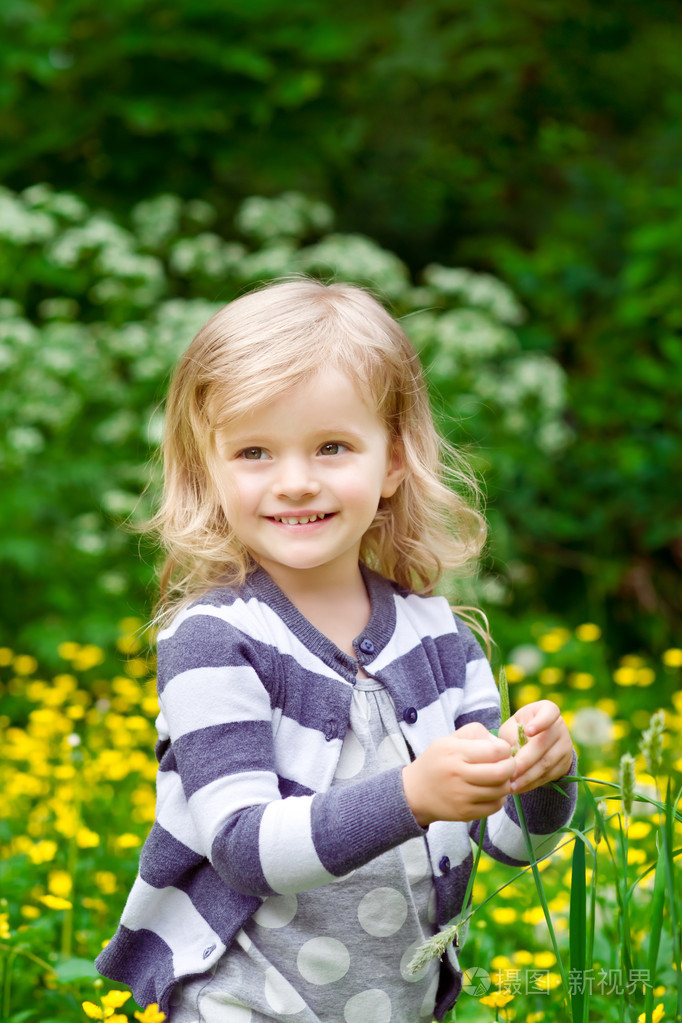可爱微笑的小女孩在她草的手在夏季的一天