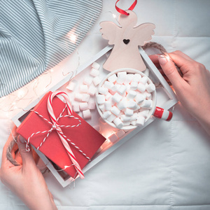 新年或圣诞节平躺顶部视图与热可可咖啡巧克力与棉花糖杯圣诞节节日庆典红色礼物盒在木托盘在床上与灯和妇女的手。方形2019