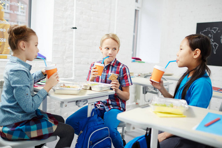 三小学同学吃桌上的午餐, 用塑料玻璃杯喝
