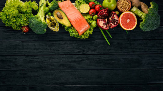 健康食品。鱼鲑, 鳄梨, 花椰菜, 新鲜蔬菜, 坚果和水果。在黑色的背景。顶部视图。复制空间