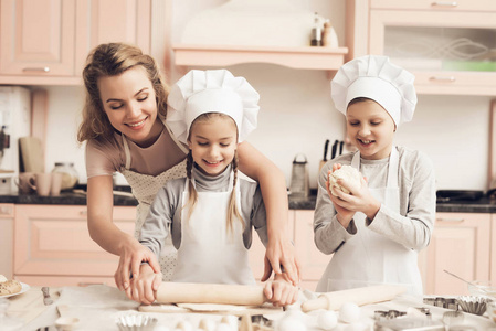 孩子在白色帽子和母亲做曲奇饼从面团在厨房