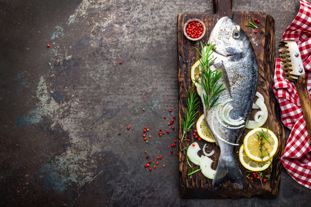用木板烹调的配料的鲜鱼。原始的海鲷或多拉达鱼在黑暗的复古金属背景。膳食食品。顶部视图
