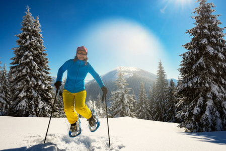 快乐的冒险家, 女人正跳上穿雪鞋, 在冬日的山上, 在一个阳光明媚的早晨, 在山谷的背景下嬉戏。背光