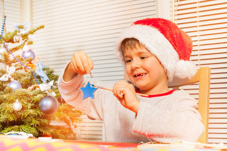 在圣诞老人的服装中的学龄前男孩的肖像举行木质圣诞明星和装饰与蓝色油漆
