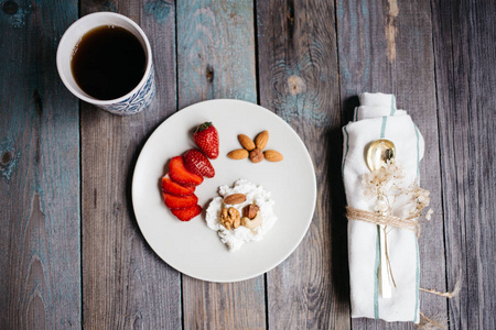 一盘有奶酪草莓和坚果的盘子一杯咖啡和一张木桌上的毛巾健康的食物早餐