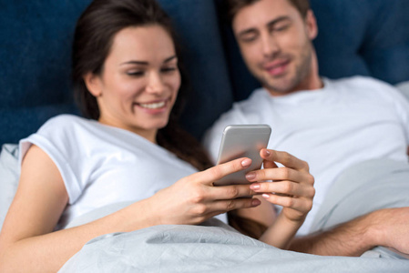 妇女使用智能手机, 而躺在床上与她的丈夫