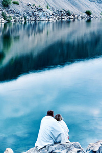 在爱的情侣在一个温暖的白色格子坐在湖的石岸边与清澈的水远离城市在清晨迎接黎明