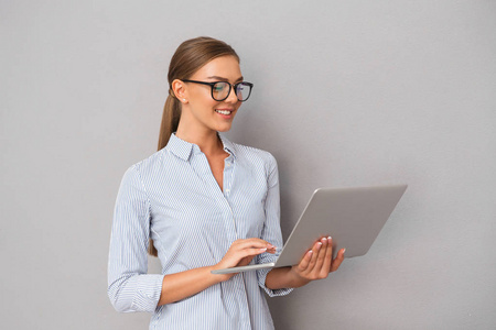 美丽的微笑的企业妇女的形象站在灰色墙背景上使用笔记本电脑