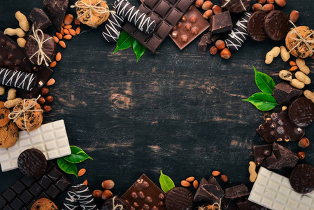 一套巧克力, 配坚果, 饼干和可可。在黑色的木质背景。顶部视图。复制文本空间