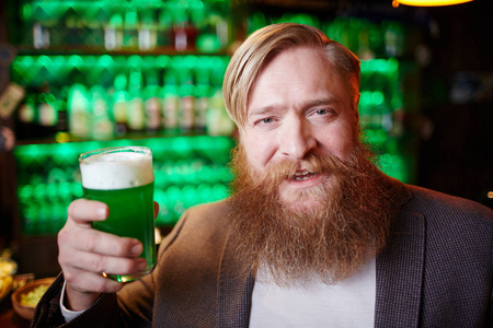 欢快的胡子人举杯与玻璃绿色泡沫啤酒在酒吧