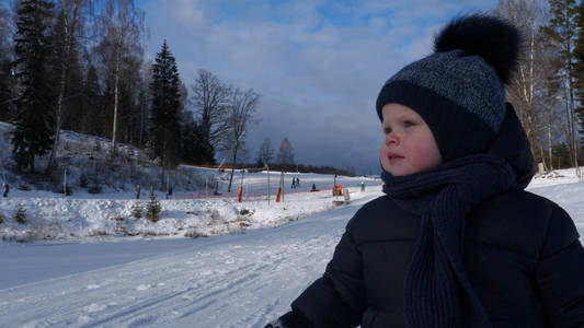 一个英俊的蹒跚学步的男孩 儿子 走过滑雪胜地的雪地, 在一个晴朗的日子里, 在冬天, 所有的雪