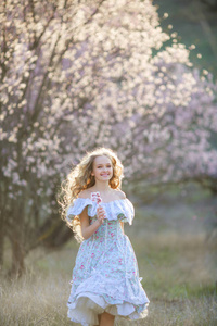 年轻美丽的金发女孩摆在盛开的花园穿着蓝色的礼服