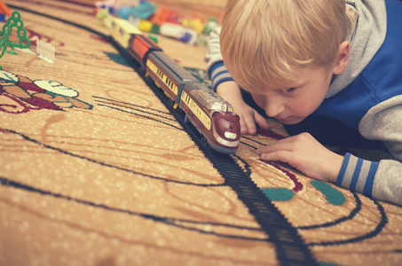 一个金发男孩在地毯上的一个房间里玩玩具火车。
