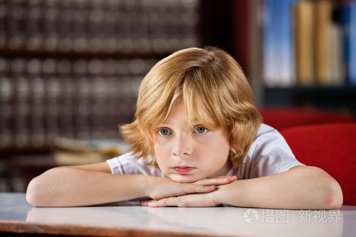 手在桌上休息下巴时东张西望的钻孔的男孩