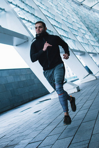 行动速度。全长的年轻男子在运动服装慢跑反对工业城市视图