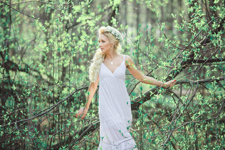 美丽的女人在白色的礼服和花卉花圈在她的头, 在开花的叶子