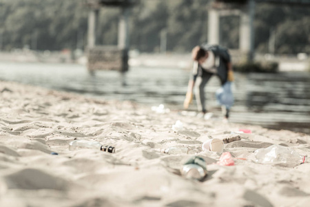 关闭的垃圾躺在沙子, 而年轻的志愿者收集它
