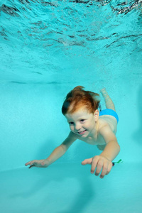 快乐的小男孩潜水水下到池底的蓝色背景和微笑。肖像。从水底射击。垂直视图