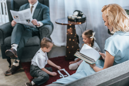 父母阅读书一份报纸, 而快乐的孩子玩多米诺瓷砖, 二十世纪五十年代风格