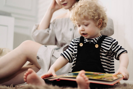 一个关心的年轻卷曲的母亲玩她的小儿子, 一个孩子读一本书