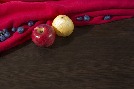 红苹果, 黄梨和蓝色的葡萄, 在木质表面有红色的窗帘