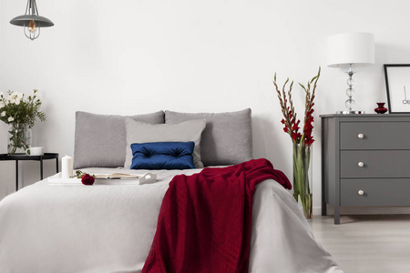 迷人的卧室内部配有一张带灰色床单和靠垫的床, 配有蓝色和红色的对比装饰。真实照片