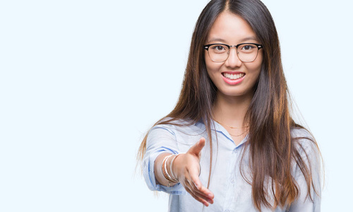 年轻的亚洲商业妇女戴着眼镜在孤立的背景微笑友好提供握手作为问候和欢迎。成功的企业