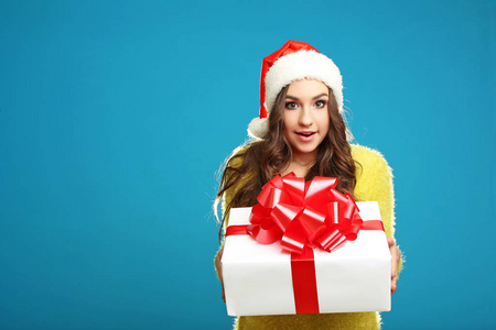 年轻的女孩在圣诞老人帽子持有礼品盒蓝色背景
